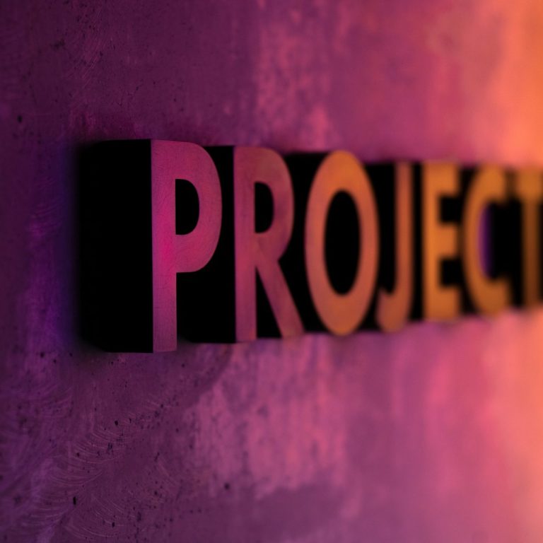 Wort PROJECT an einer Wand mit violett-oranger Lichtstimmung – abstrakte Darstellung für Projektarbeit oder Transformation