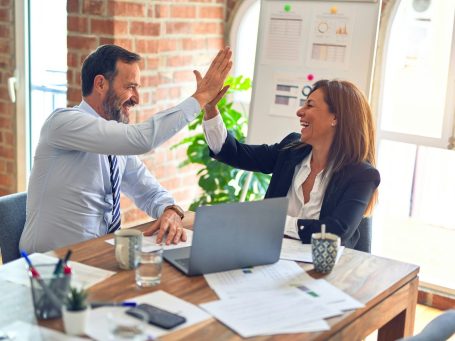 Zwei Businesspersonen geben sich ein High-Five in einem modernen Büro – Sinnbild für erfolgreiche Zusammenarbeit und positive Dynamik