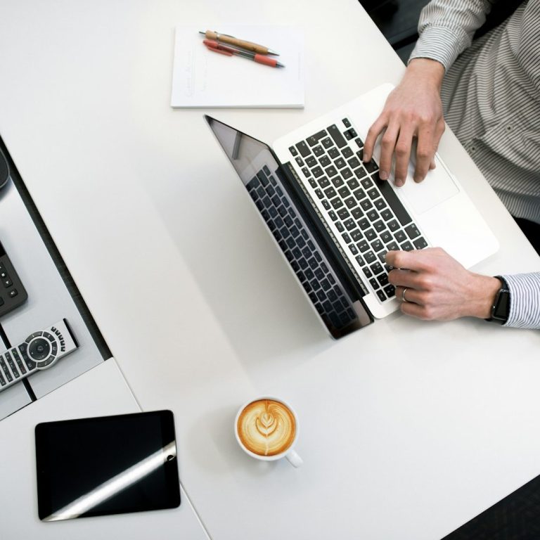 Person arbeitet am Laptop mit Tablet, Notizblock und Kaffee – Sinnbild für modernes, digitales Arbeiten im Beratungsumfeld.
